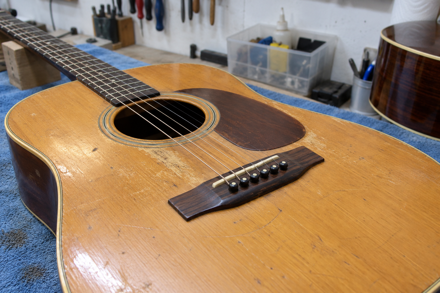 Een oude akoestische gitaar ligt op een gewone werkbank met een blauwe handdoek.